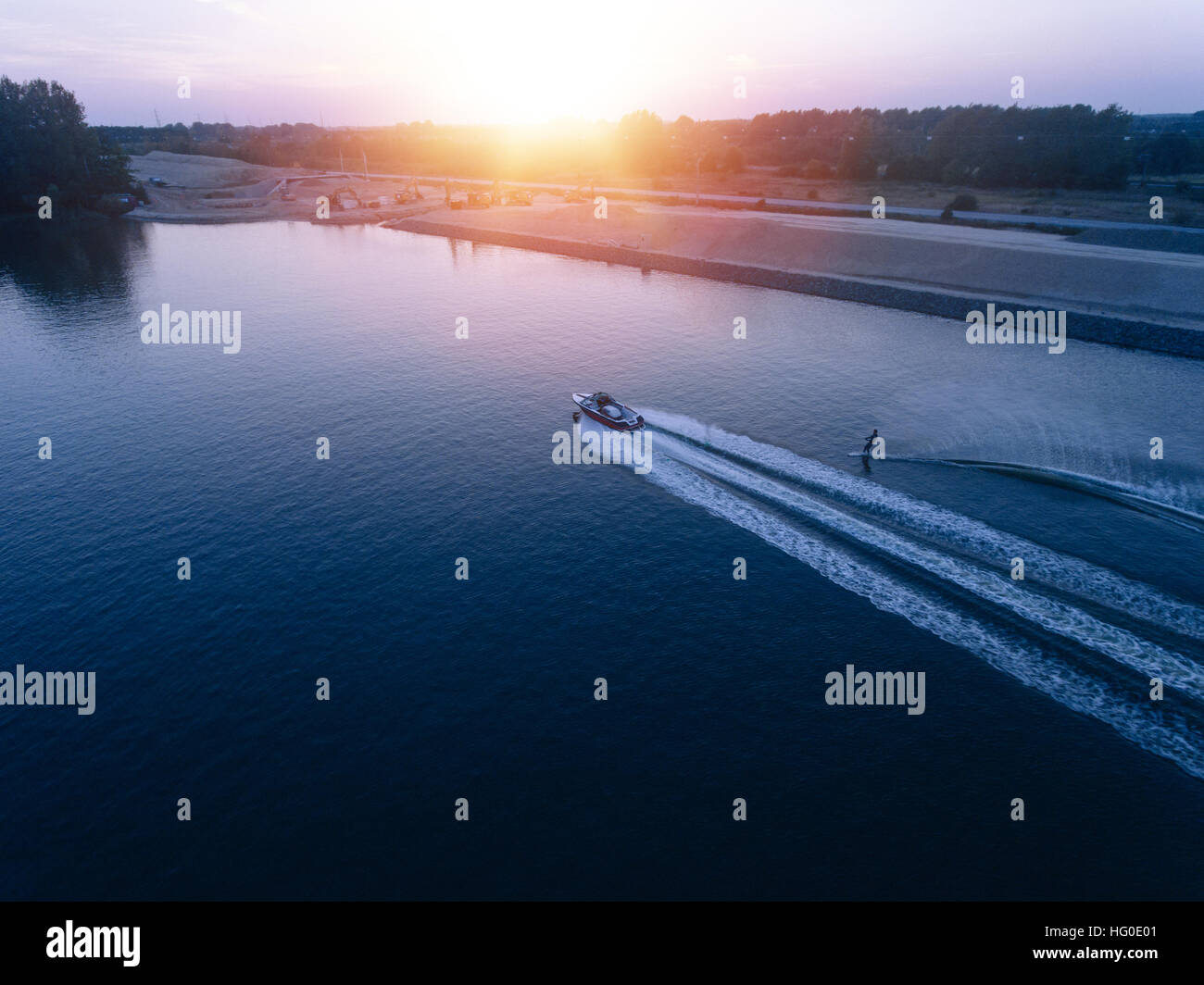 Aerial view of man water skiing on lake behind boat. Man wakeboarding at sunset. Stock Photo