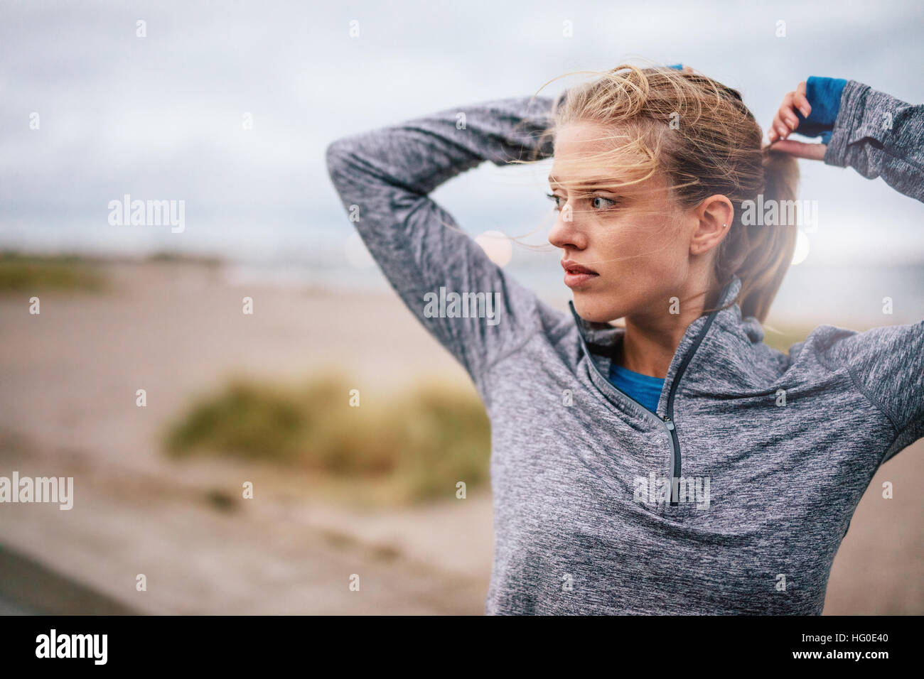 Close up of young female runner tying up hair before a run. Sporty fitness woman on outdoor workout looking away. Stock Photo