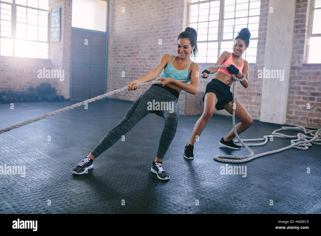 Shot of two strong young women doing rope pulling exercises at a gym. Fitness females pulling rope at gym and smiling. Stock Photo