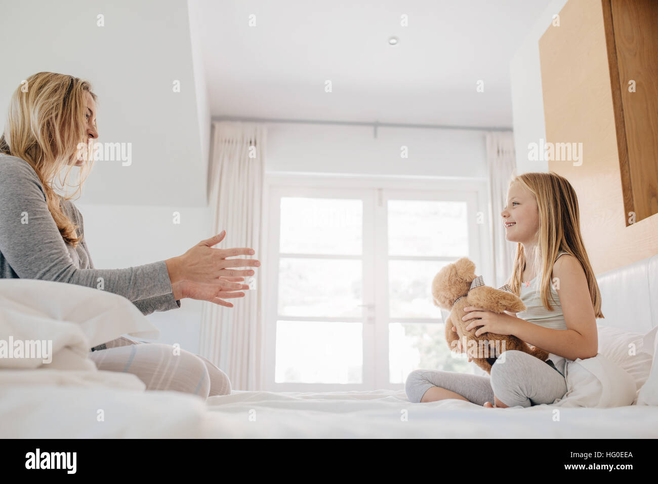 Shot of little girl and woman playing with teddy bear. Mother and daughter playing with teddy bear on bed at home. Stock Photo