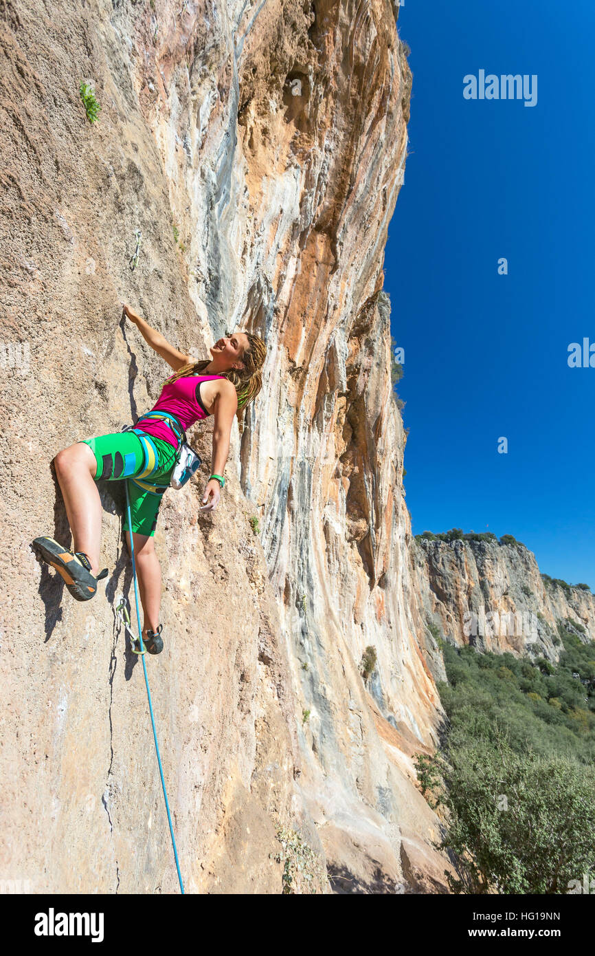 Jolly Young Girl hanging on vertical rocky Wall sunny Landscape Stock Photo