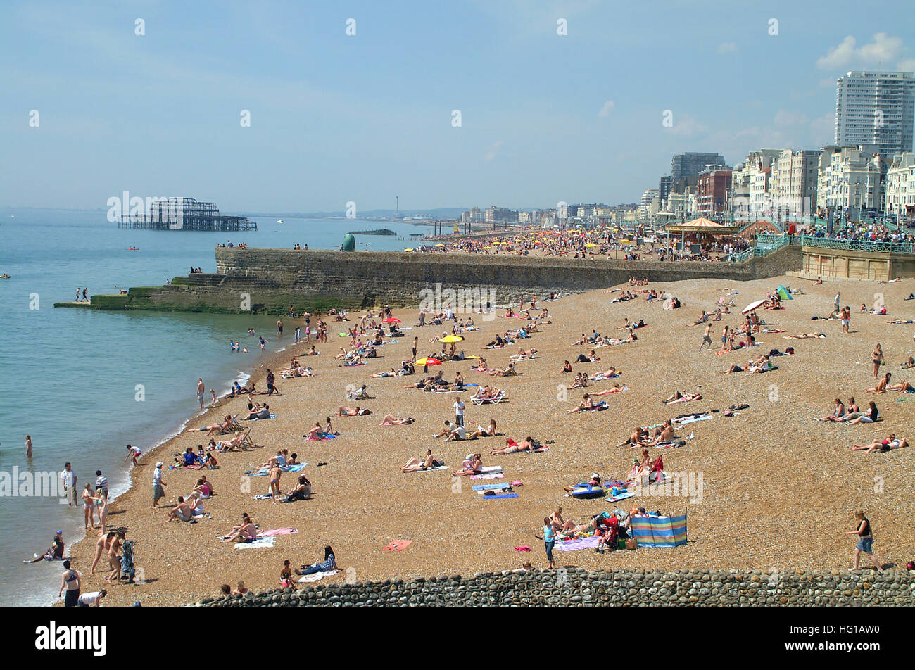People on Brighton beach between sea defense groynes and the ruins of Old West pier in the background, Sussex, England. Stock Photo