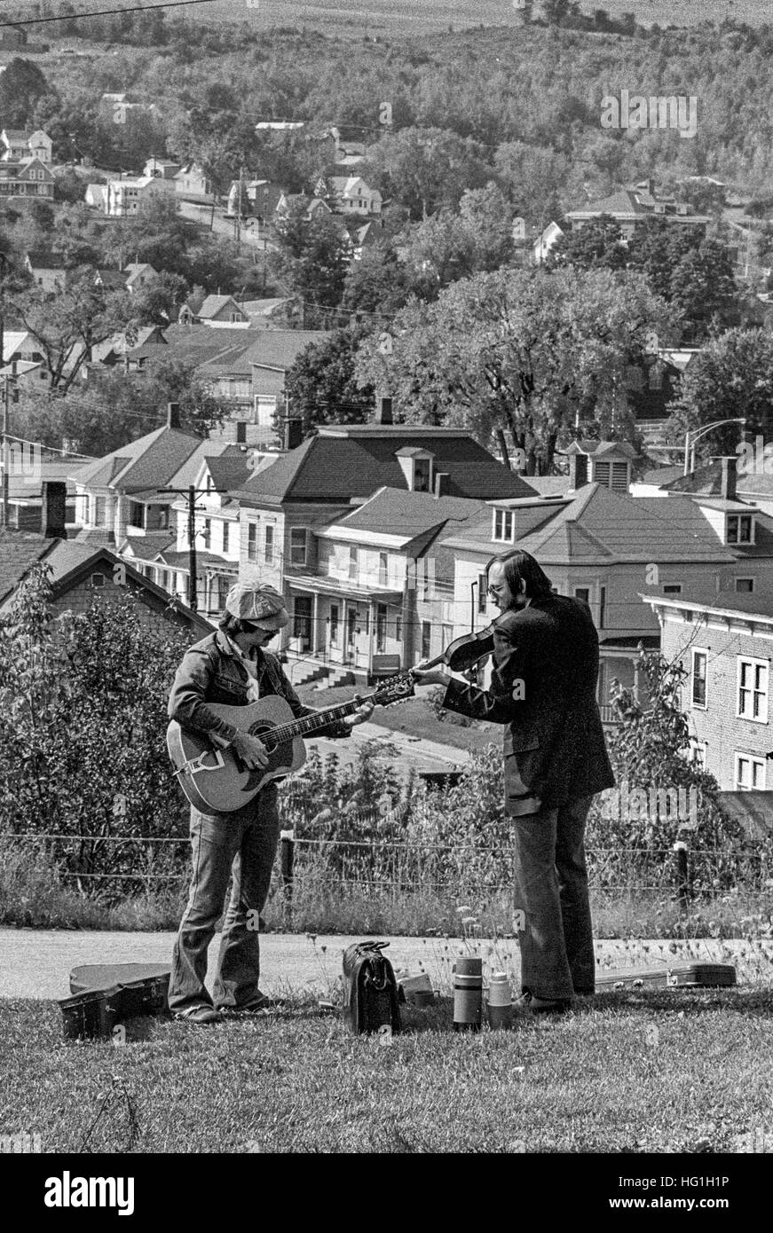 Playing guitar and violin, two musicians practice on a Vermont hillside at a folk music festival and contest. Note homes in background. Stock Photo