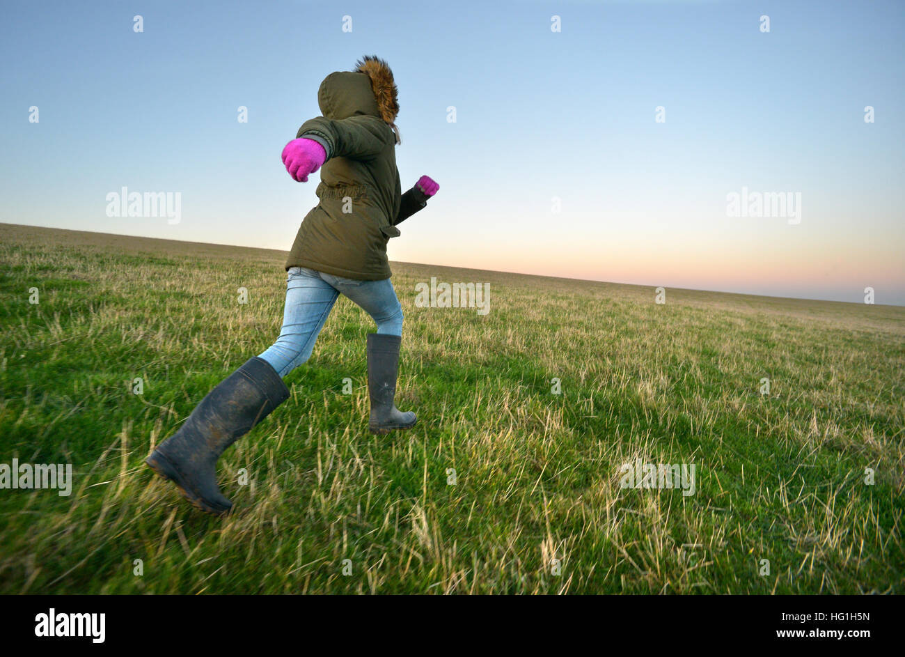 Child in welly boots running on a grassy hill Stock Photo
