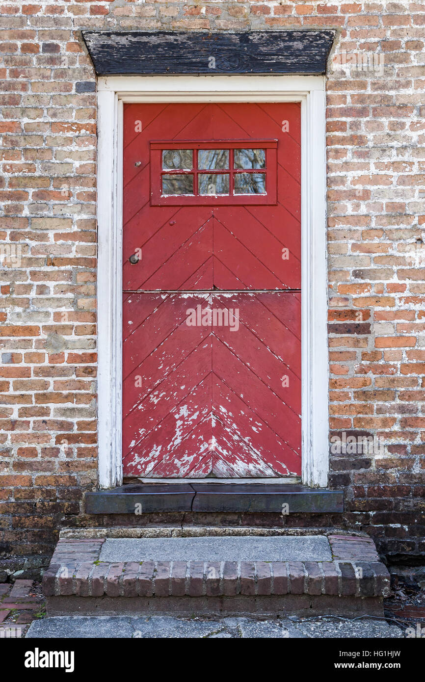 An old red door is closed on a brick building. The paint is peeling and in decay. Stock Photo