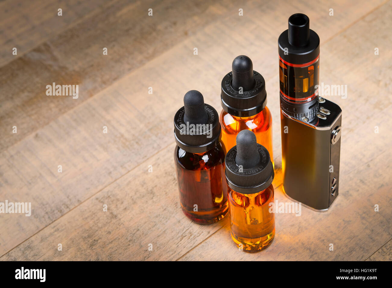 Vaping mod e-cig with tank atomizer and juice bottles over wood background Stock Photo