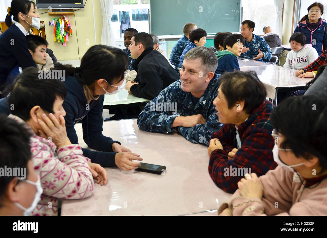 150303-N-WZ747-048 - SASEBO, Japan (March 3, 2015) Electronics Technician 3rd Class Jay Cogger, center, a Sailor assigned to the submarine tender USS Frank Cable (AS 40), shares photos of his family to residents of the Sakuraga Oka Challenged Home (SOCH), March 3.  Frank Cable Sailors and civilian mariners took part in a community service event to exchange cultural interactions with residents from the SOCH, a center dedicated to the support and well-being of challenged Japanese citizens.  Frank Cable, forward deployed to the island of Guam, conducts maintenance and support of submarines and su Stock Photo