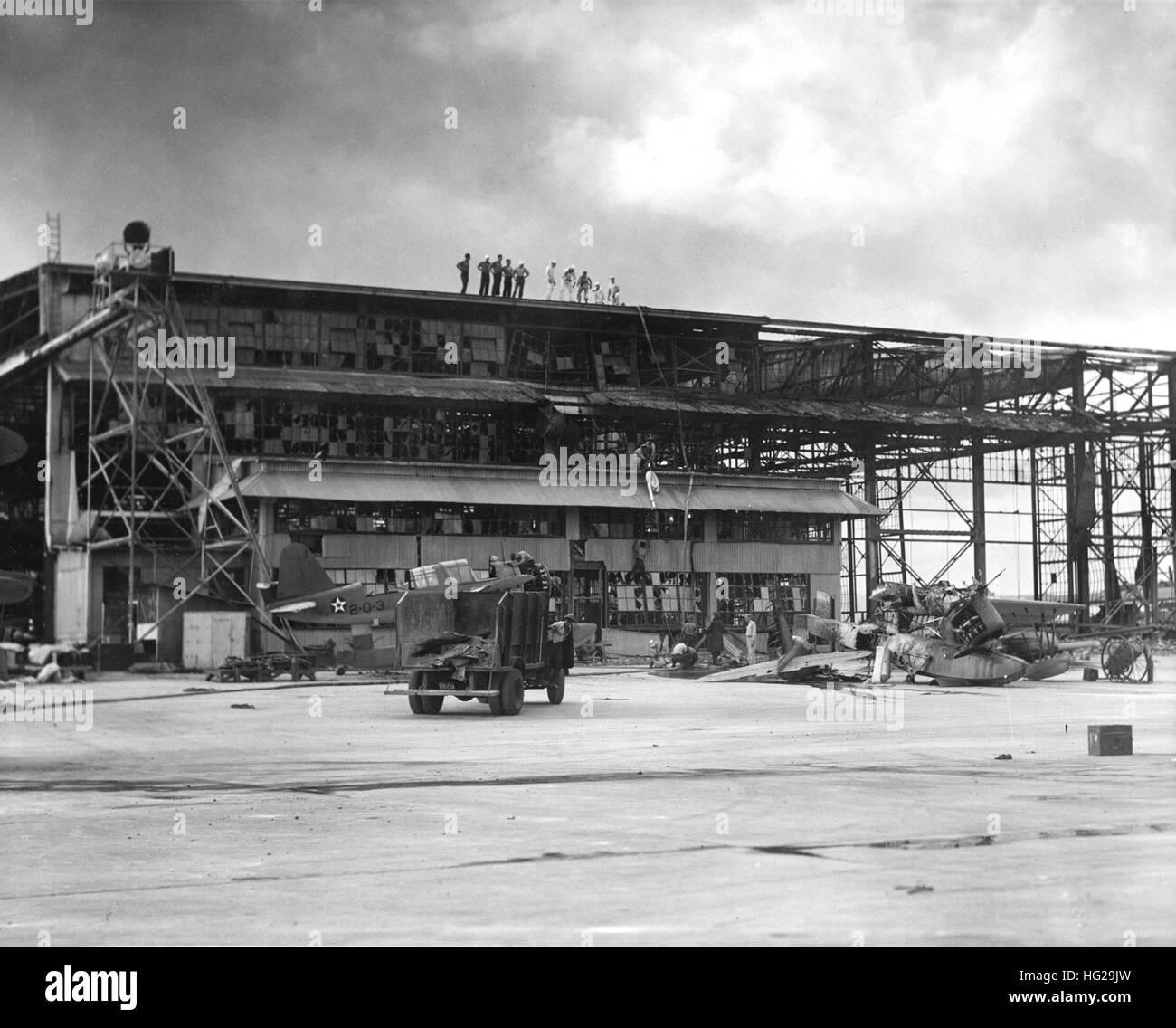 Wrecked hangar at the Ford Island Naval Air Station seaplane base on 8 December 1941, the day after the Japanese air attack. In the right foreground is a destroyed OS2U floatplane. Another OS2U (marked 2-O-3) is under repair to the left. Official U.S. Navy Photograph, now in the collections of the National Archives. Wrecked hangar at NAS Ford Island with OS2Us 1941 Stock Photo