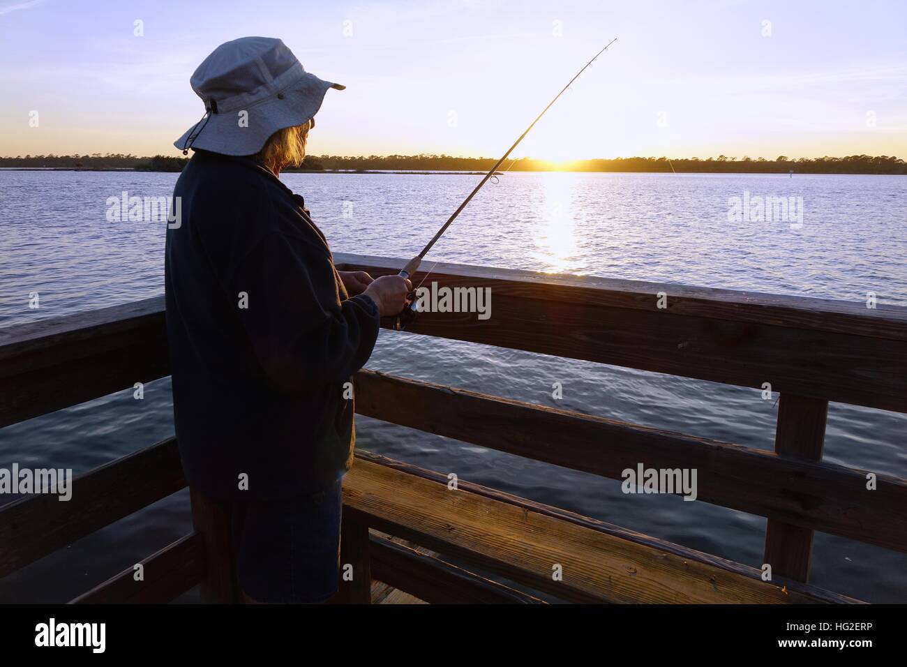 Woman fishing from a dock on the Halifax River at sunset. Ormond Beach