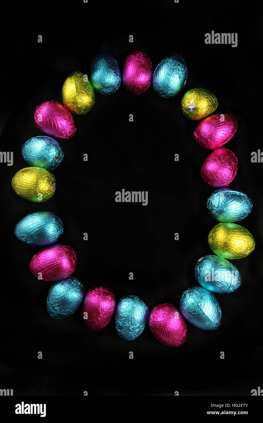 Colorful foil wrapped easter eggs laid out in the oval shape of an egg, on a black background. Stock Photo