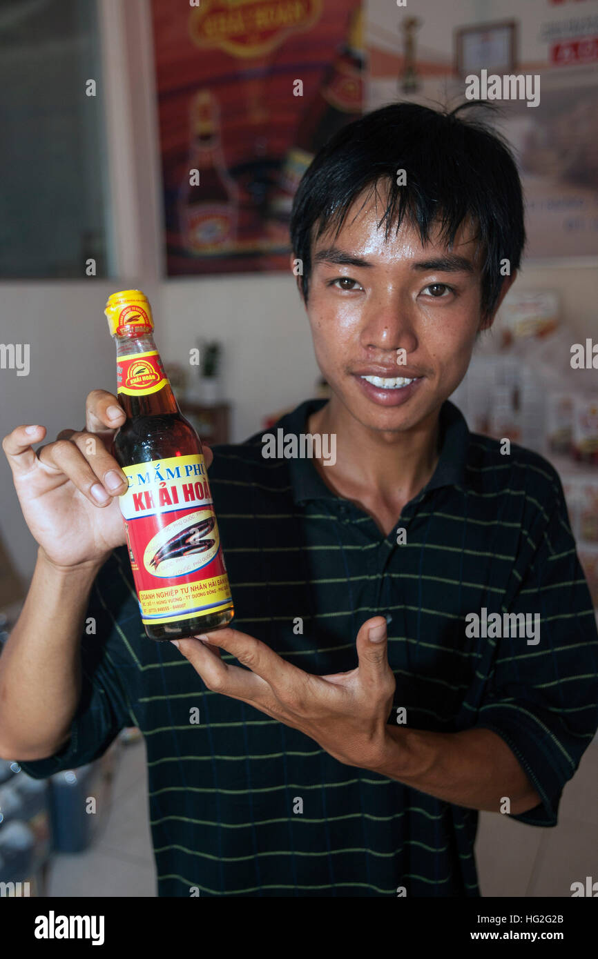 Young man with bottle of fish sauce at fermentation plant Duong Dong town Phu Quoc island Vietnam Stock Photo