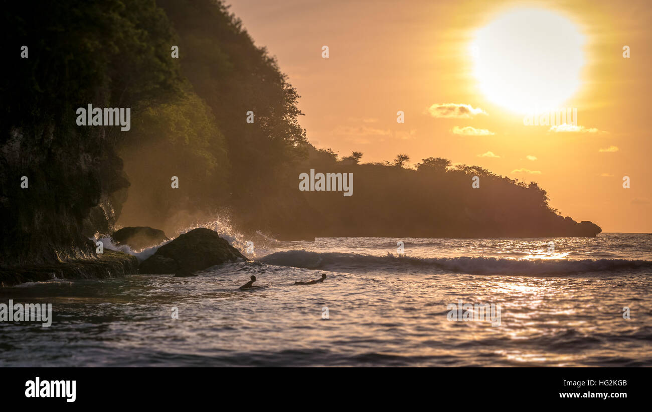Local Kids surf on Waves in Sunset light, Beautiful Crystal Bay, Nusa Penida Bali Stock Photo