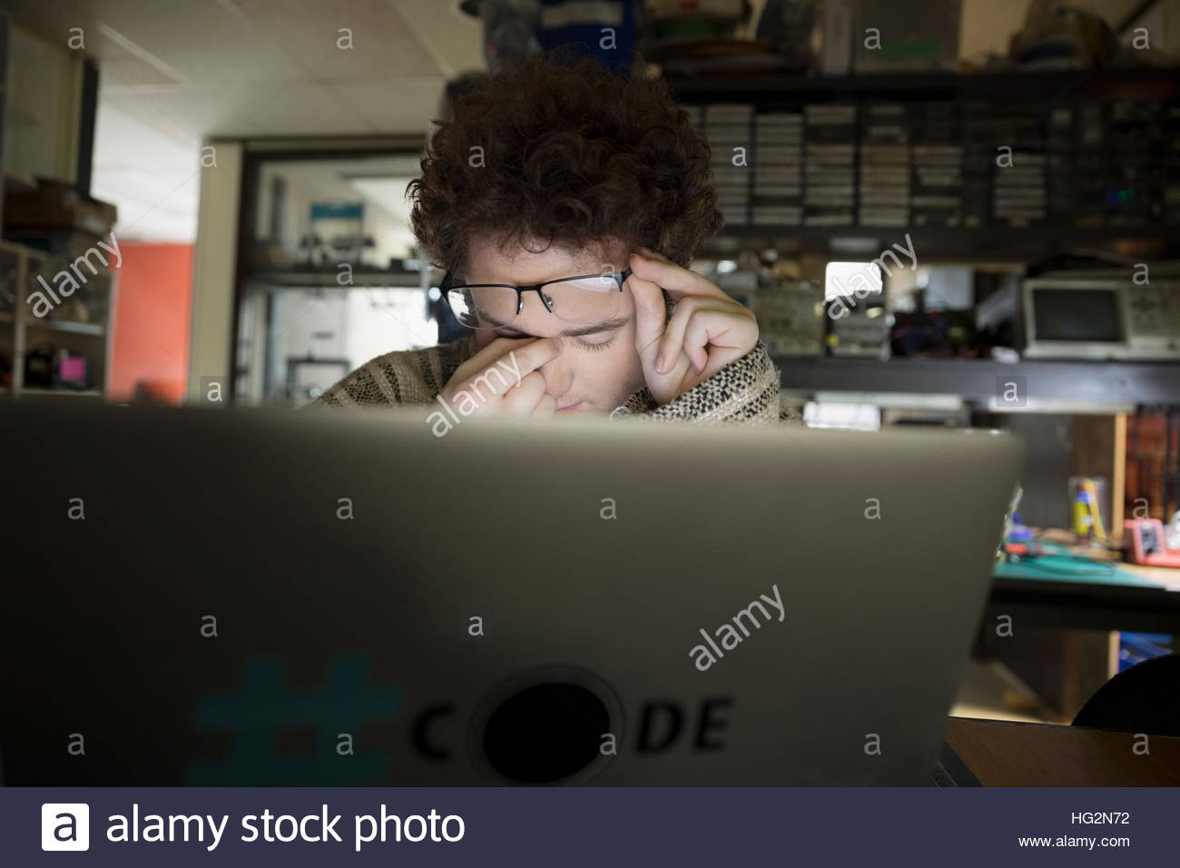 Exhausted computer programmer at laptop in dark workshop Stock Photo