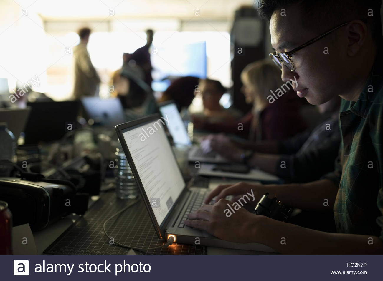 Focused male hacker working hackathon at laptop in dark office Stock Photo