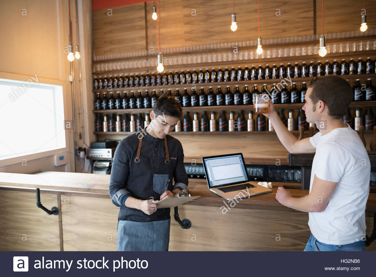 Male Brewers With Clipboard And Laptop Examining Beer In