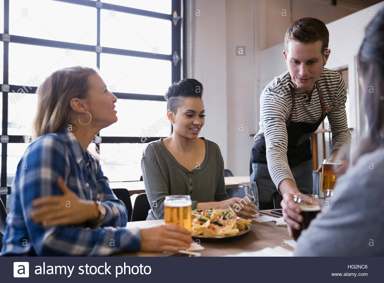 Waiter serving beers to women friends at brewery restaurant table Stock Photo
