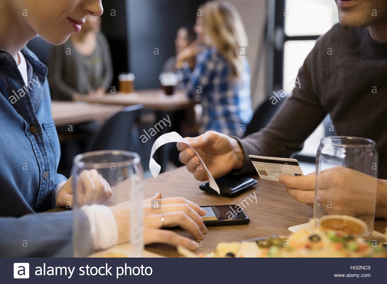 Close up couple with credit card paying bill calculating tip with smart phone in brewery restaurant Stock Photo