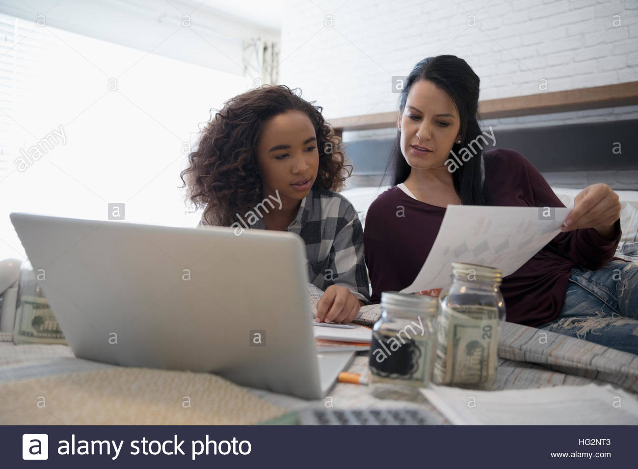 Mother with laptop teaching daughter personal finance management on bed Stock Photo