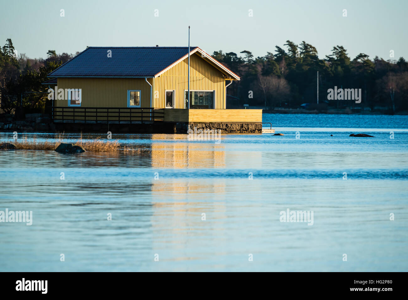 Ronneby, Sweden - January 2, 2017: Documentary of coastal lifestyle. Coastal landscape with yellow house on granite foundation in the sea. Windless mo Stock Photo