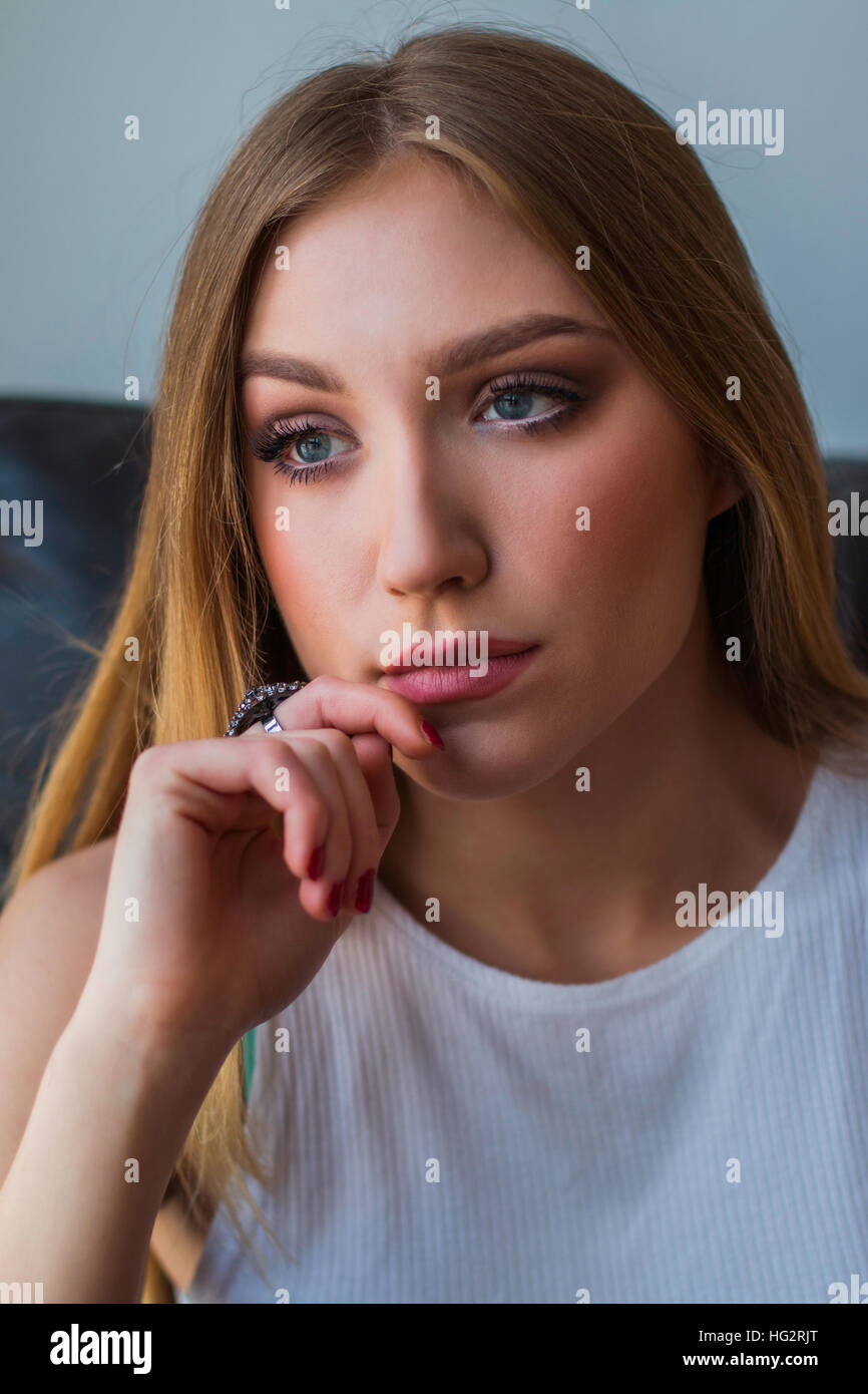 Young woman sitting in chair, holding hand on chin, looking smart and thoughtful Stock Photo