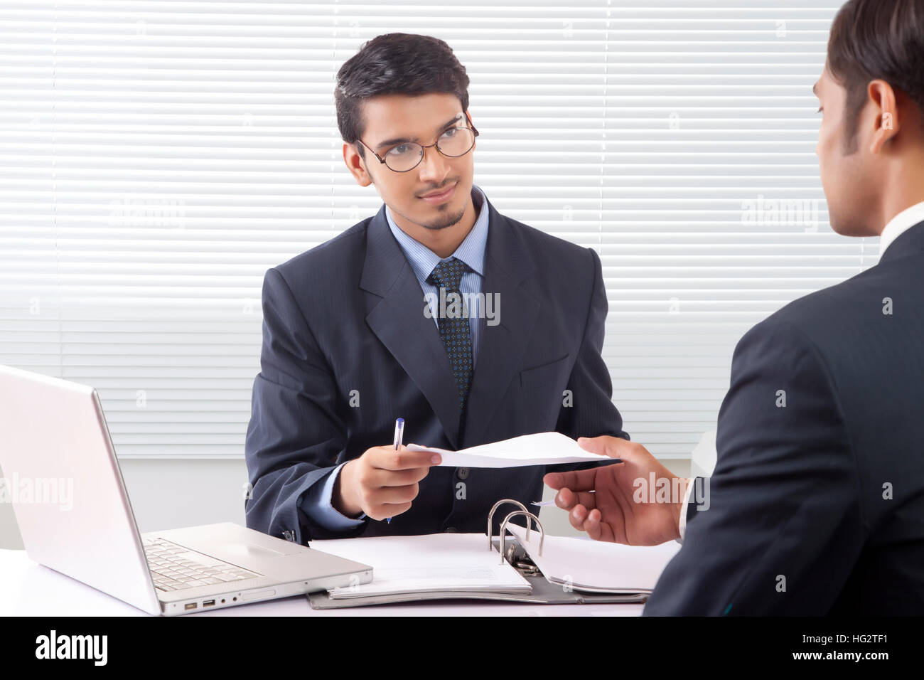 Young professional man giving document to another professional man inside office cabin Stock Photo