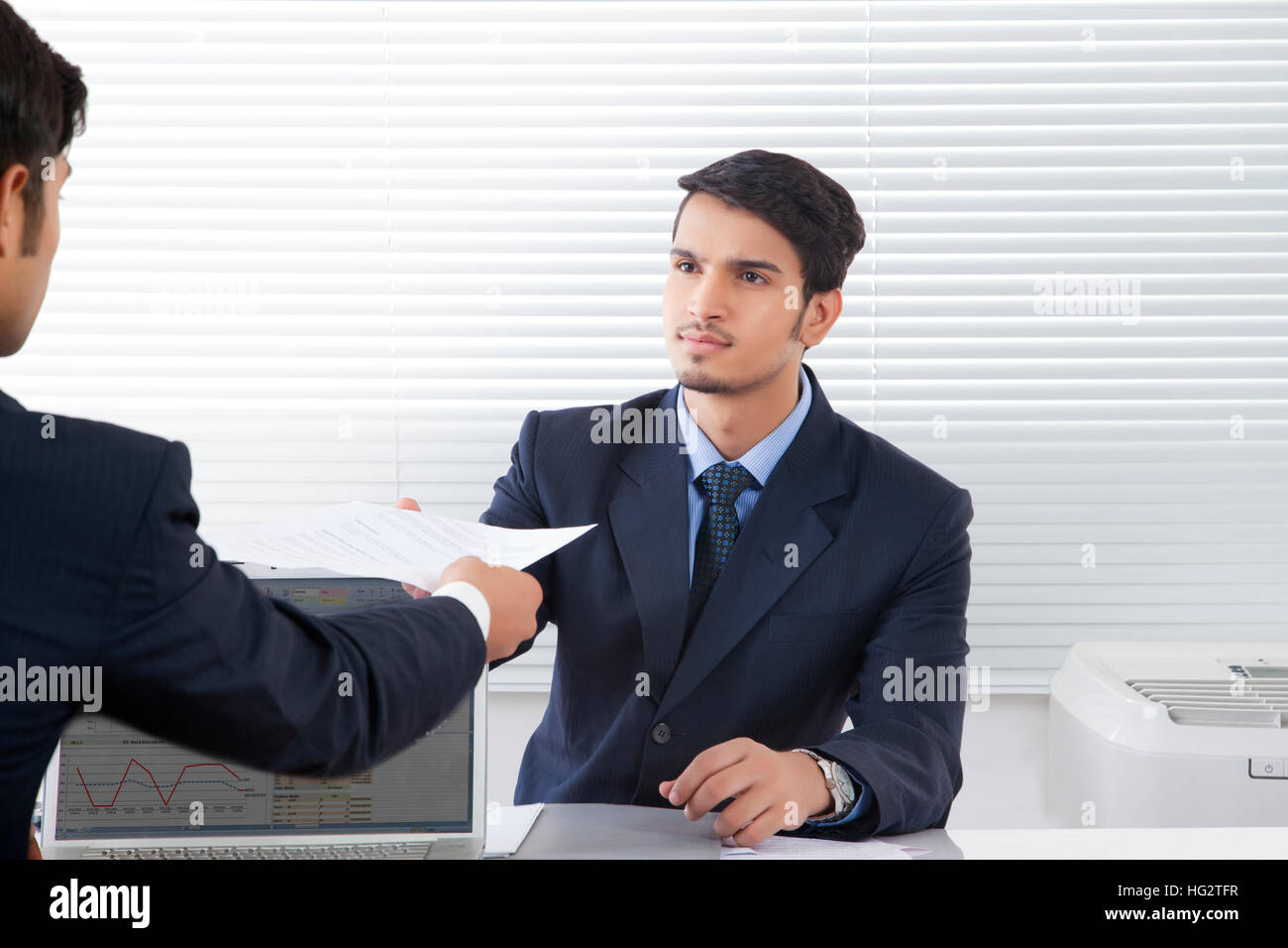 Businessman handing over document to young professional man in office Stock Photo