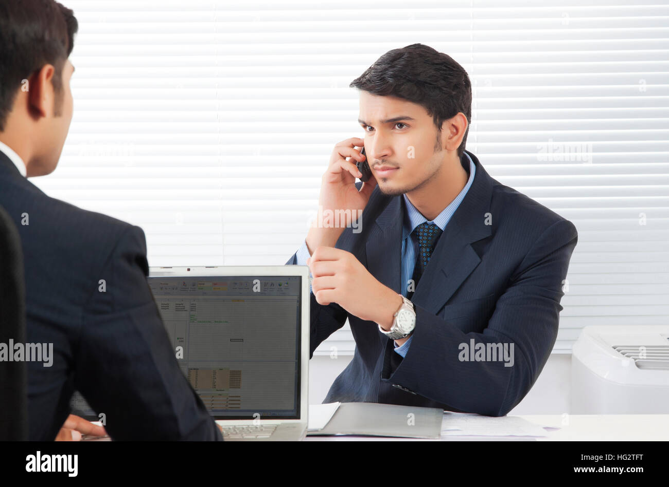 Businessman talking over mobile phone while discussing work with colleague in office Stock Photo