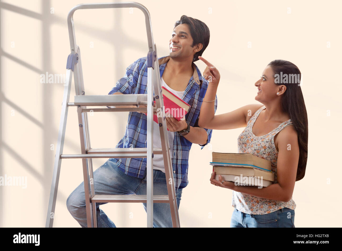 Portrait of a young couple carrying books standing on ladder Stock ...