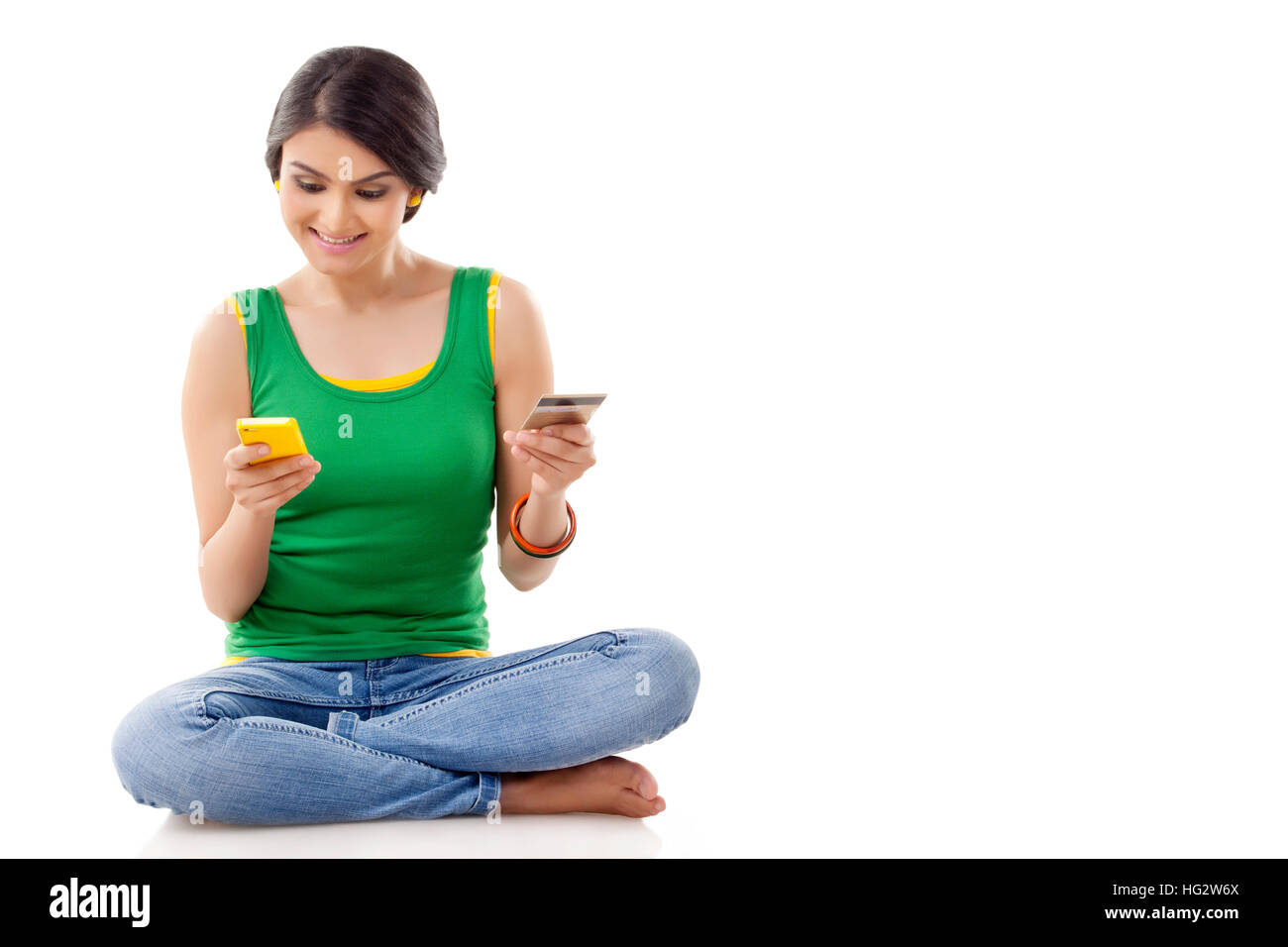 Portrait of a young woman  sitting on floor and holding a mobile phone and a credit card Stock Photo