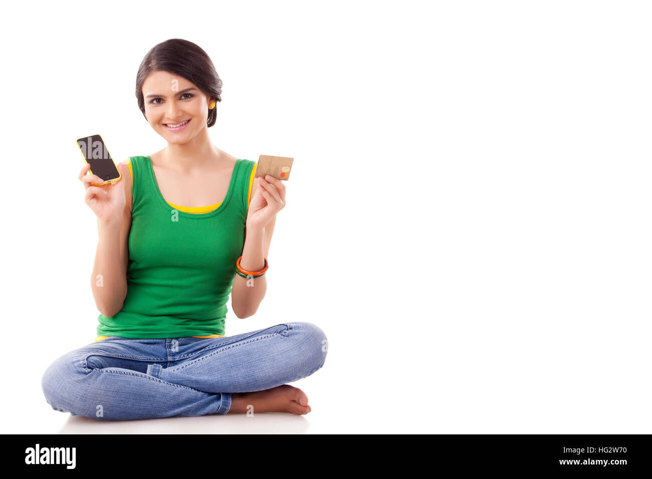 Portrait of a young woman  sitting on floor and holding a mobile phone and a credit card Stock Photo