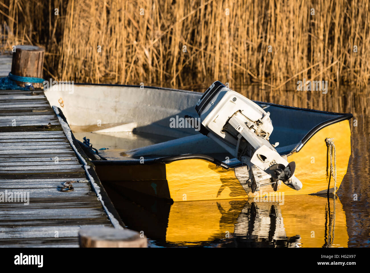 Yellow motorboat moored at wooden pier on cold and frosty morning. Boat is full of icy water. Motor lifted from the sea. Stock Photo