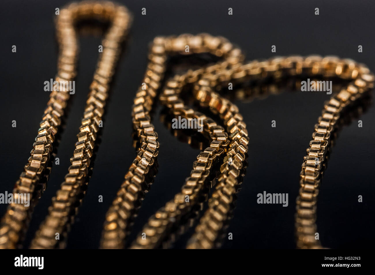 Gold necklace chain closeup jewellery reflecting on glass table Stock Photo