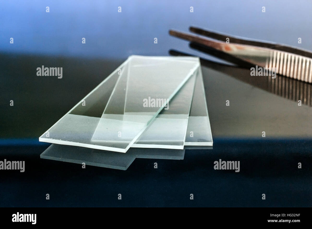 Microscope glass slides reflecting on glass table with pliers on the