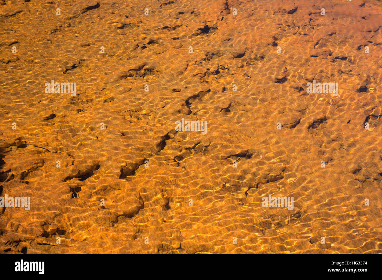 Closeup of a reddish-orange stream flowing into Hot Lake in Yellowstone National Park. Stock Photo