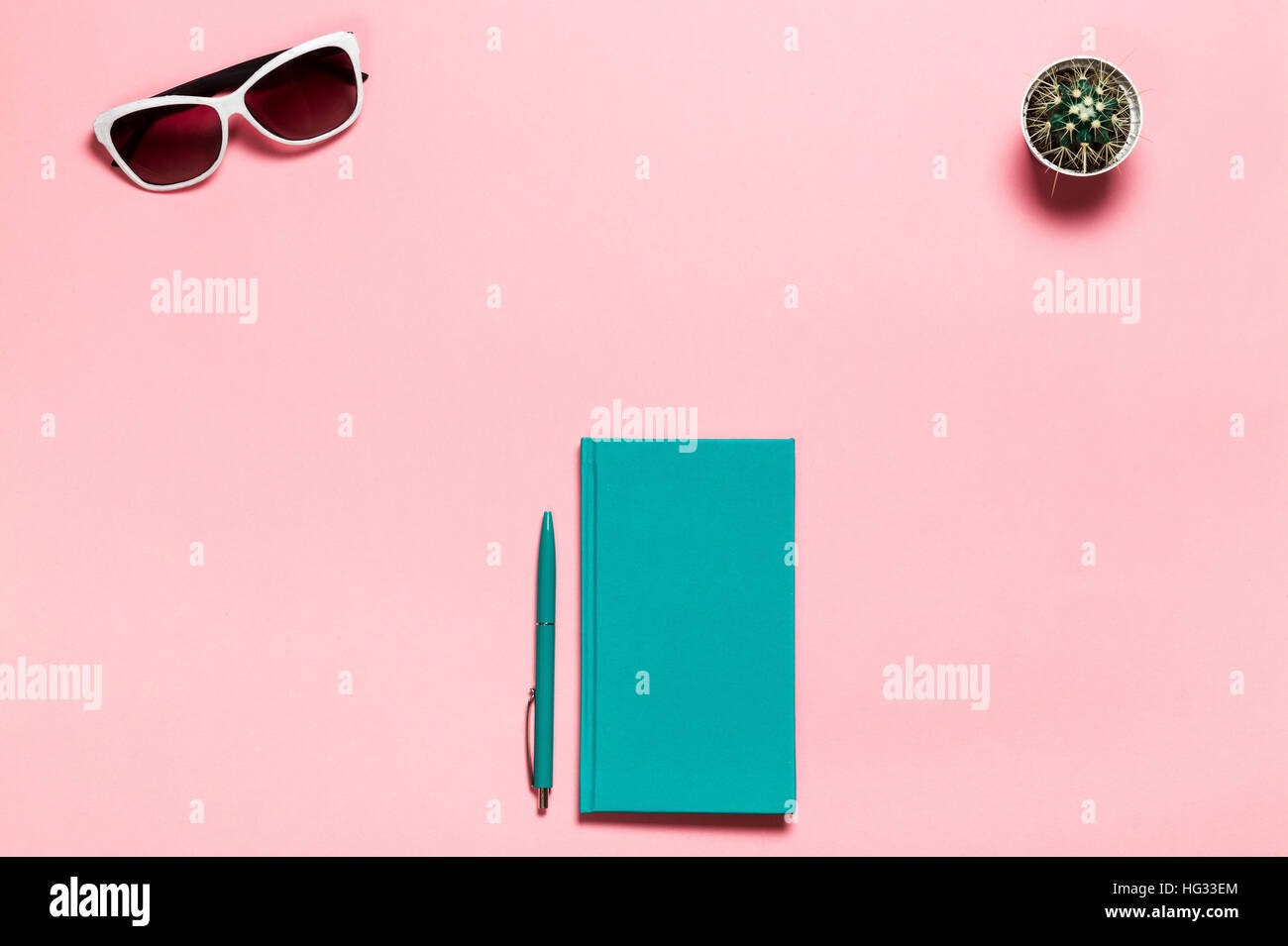 Creative flat lay photo of workspace desk with aquamarine notebook, eyeglasses, cactus copy space pink background, minimal style Stock Photo