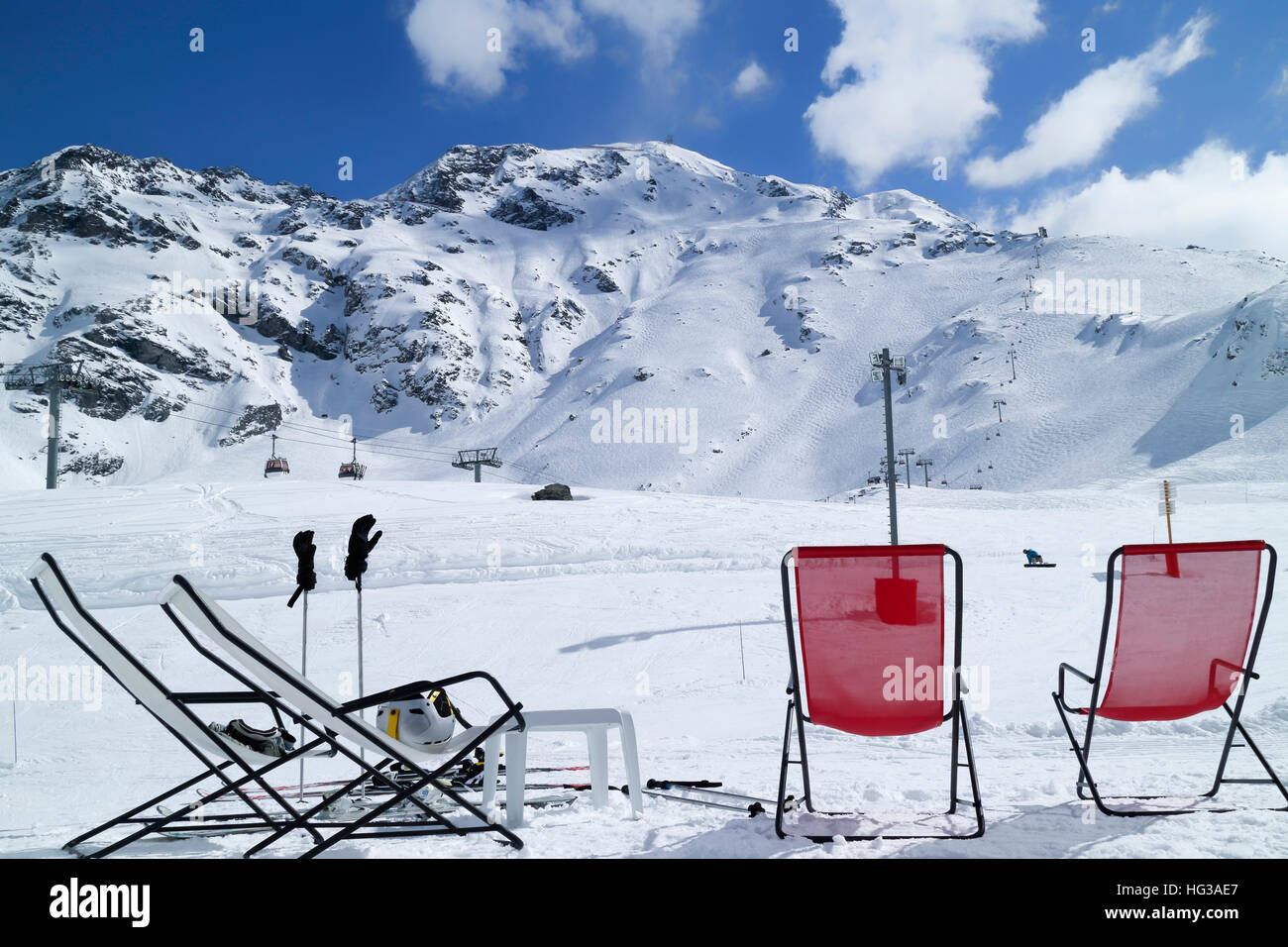 Red and white relaxing lounge chairs on snow in front of ski piste and lifts, in alpine winter resort of Les Arcs, France . Stock Photo
