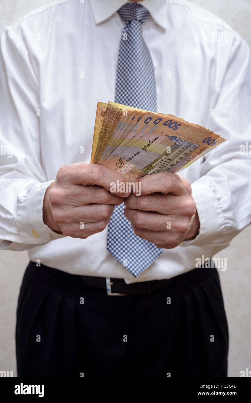 Corrupted businessman, or politician, counting and offering a Hryvnia banknotes bribe, in Ukraine Stock Photo