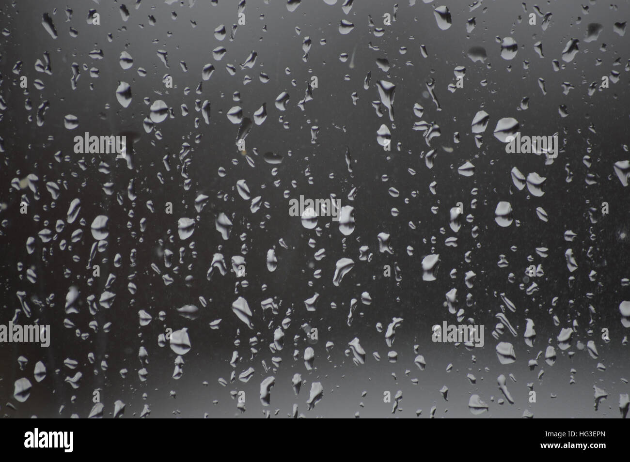 The image shows the pane only and background is darker and the raindrops lighter.   The rain drops are even over the glass. Stock Photo