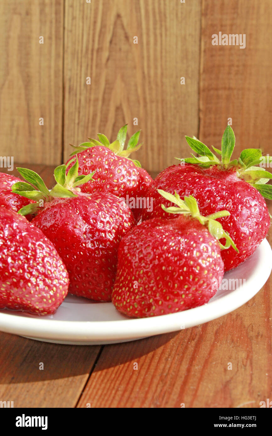 ripe red strawberries on the white plate on the brown background. Red strawberry on the plate. Stock Photo