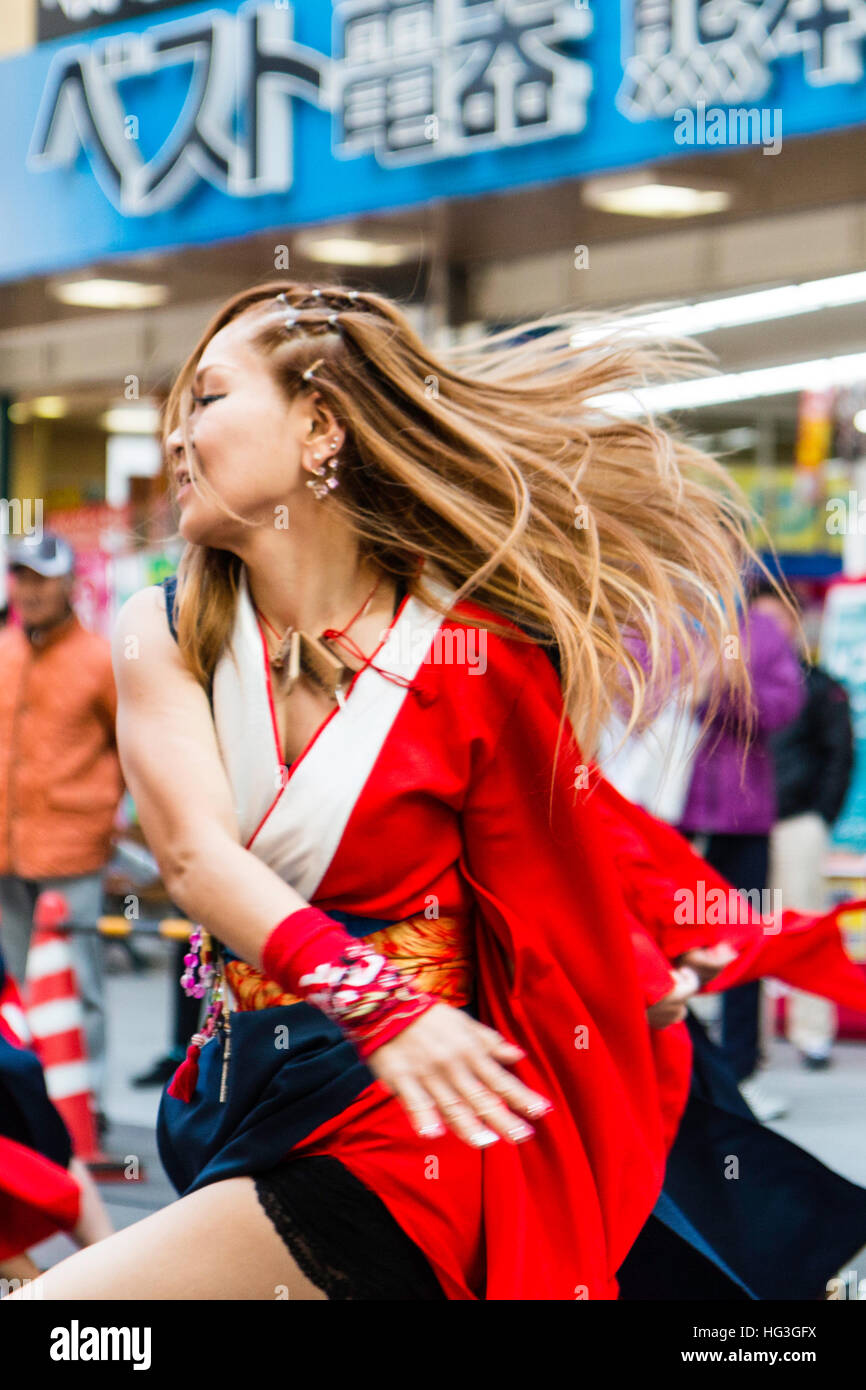 Yosakoi festival. Japanese women dancer with dyed red hair, dancing in city shopping arcade, swirling with her hair flying, blurred motion. Stock Photo