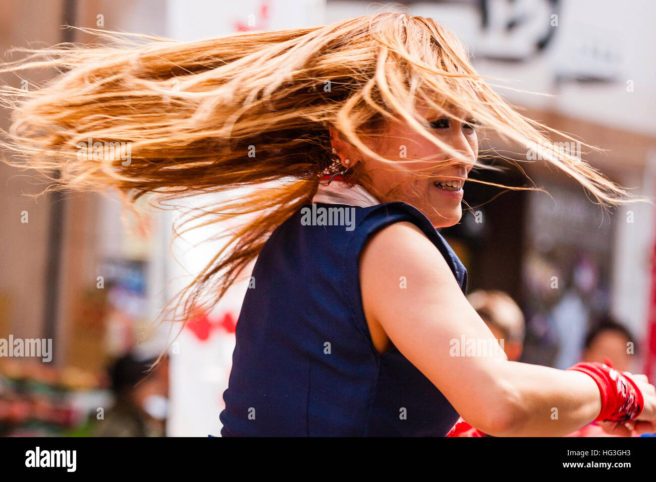 Yosakoi festival. Japanese women dancer with dyed red hair, dancing in city shopping arcade, swirling with her hair flying, blurred motion Stock Photo