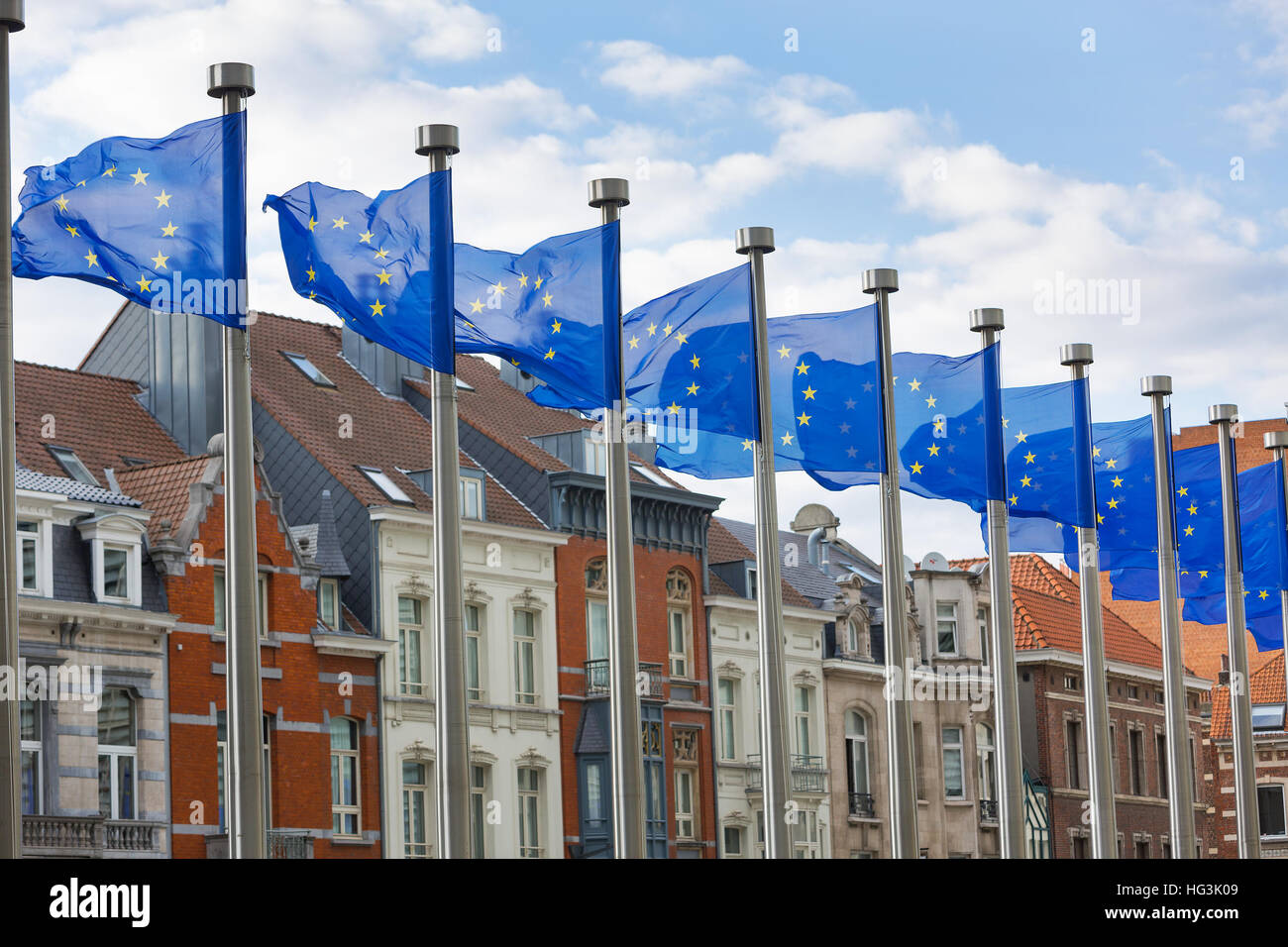 A line of EU flags flying on metal poles in front of the Berlaymont Building in Brussels with traditional houses in the background. Stock Photo
