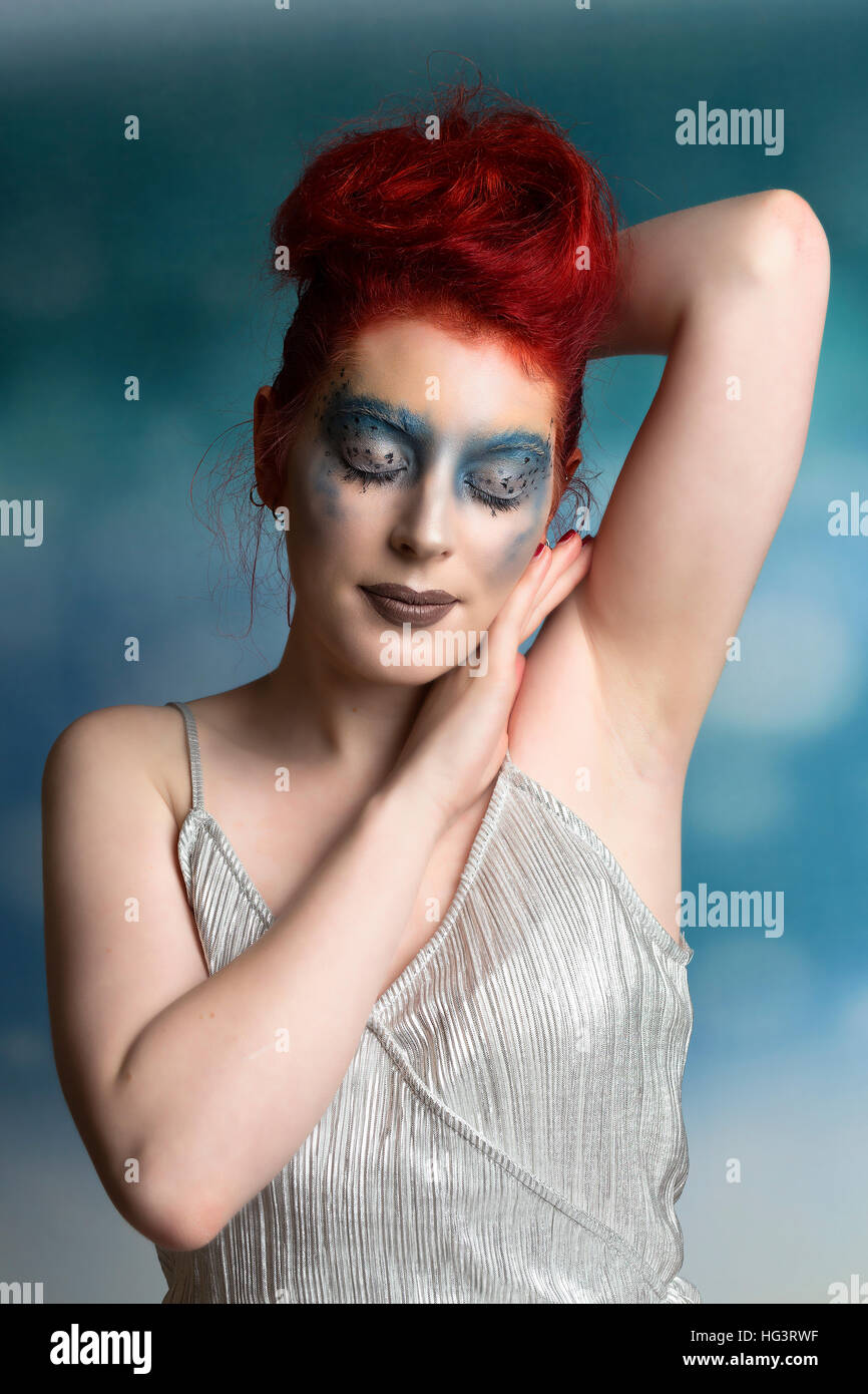 Red haired model with blue creative makeup wearing silver jumpsuit Stock Photo
