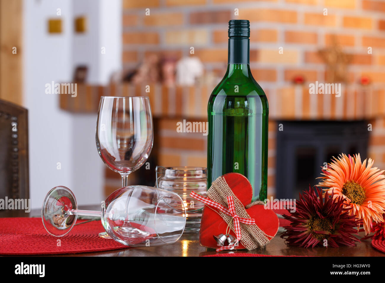 Still life with wine bottles, glasses, flowers and heart symbol, on the background a brick fireplace Stock Photo