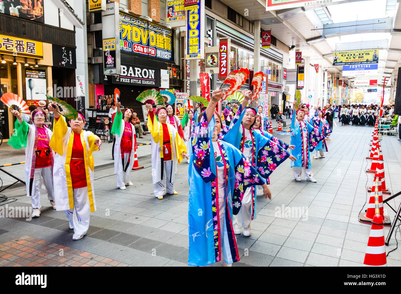 Japanese Yosakoi festival. Three rows of mature women in colourful happi coats, jackets, dancing and holding fans in shopping arcade. Stock Photo