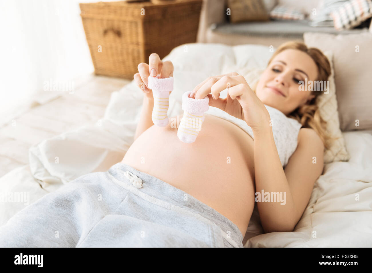 Pregnant woman holding baby socks in bed Stock Photo