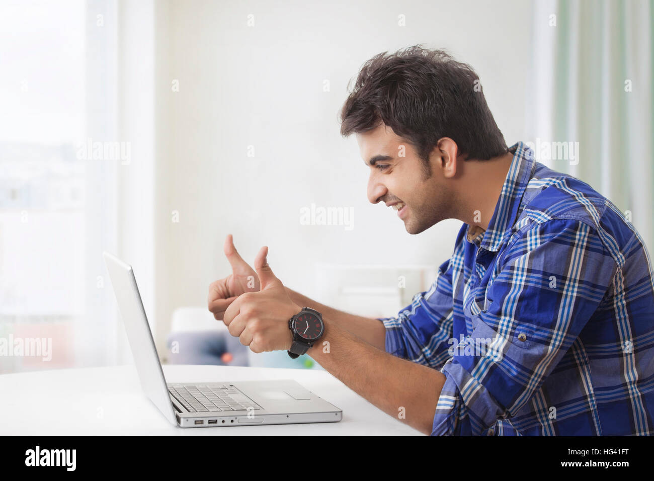 Smiling man showing thumbs up while using laptop computer Stock Photo ...