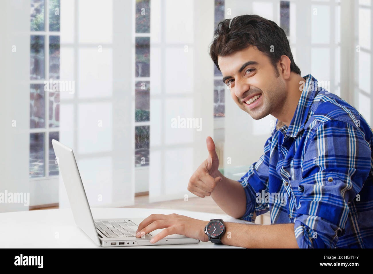 Smiling man showing thumbs up while using laptop computer Stock Photo ...