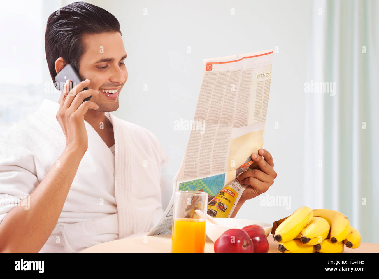 Man talking on phone and reading newspaper at breakfast table Stock Photo