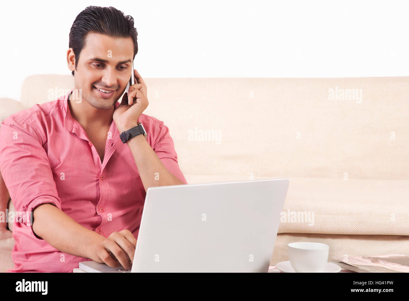 Young man talking on mobile phone while using laptop Stock Photo
